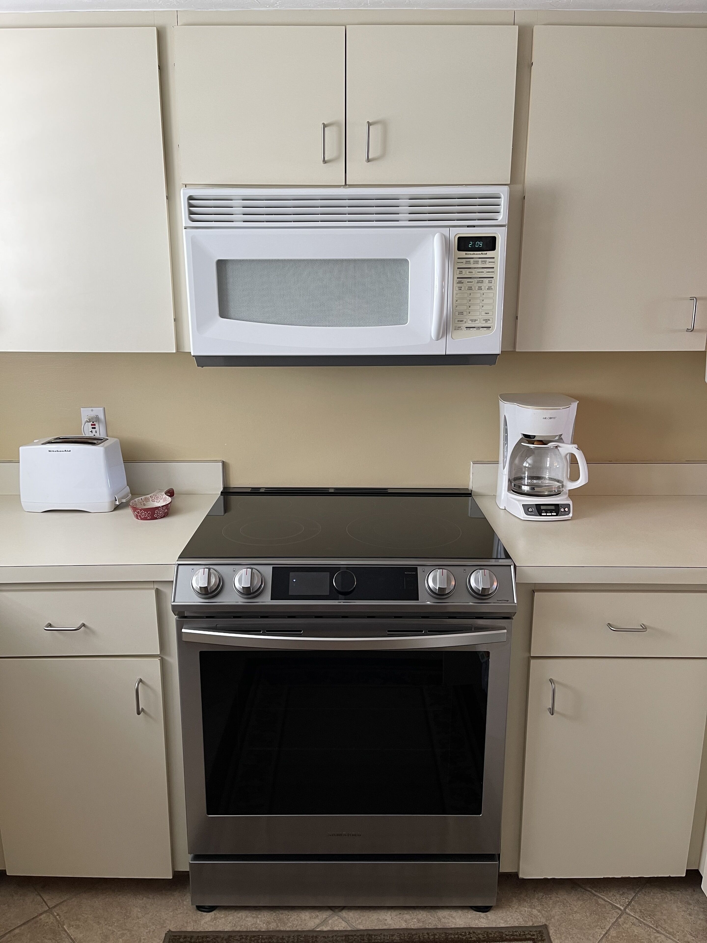 A kitchen with a microwave, toaster, coffee maker, and a stainless steel oven.