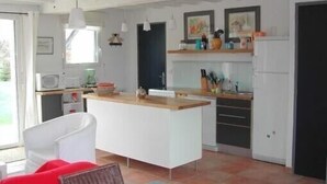 Une cuisine moderne avec des meubles blancs, un plan de travail en bois et un four encastré. On y trouve également un coin repas avec une chaise blanche et un coussin rouge.