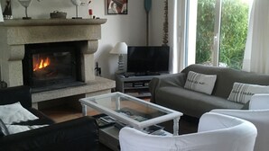 Un salon avec une cheminée en pierre, un canapé, un fauteuil blanc et un téléviseur.