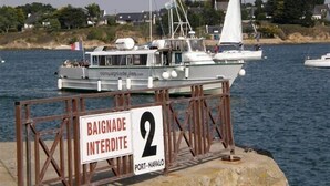 Un bateau était amarré à un quai, et une pancarte indiquait : « BAIGNADE INTERDITE À PORT-NAVALO ».