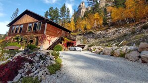 A wooden cabin with a gravel driveway, surrounded by autumn foliage and rocky terrain. - Spearfish canyon vacation home 15 minutes from Terry Peak Ski Area & Deadwood. (Lead)