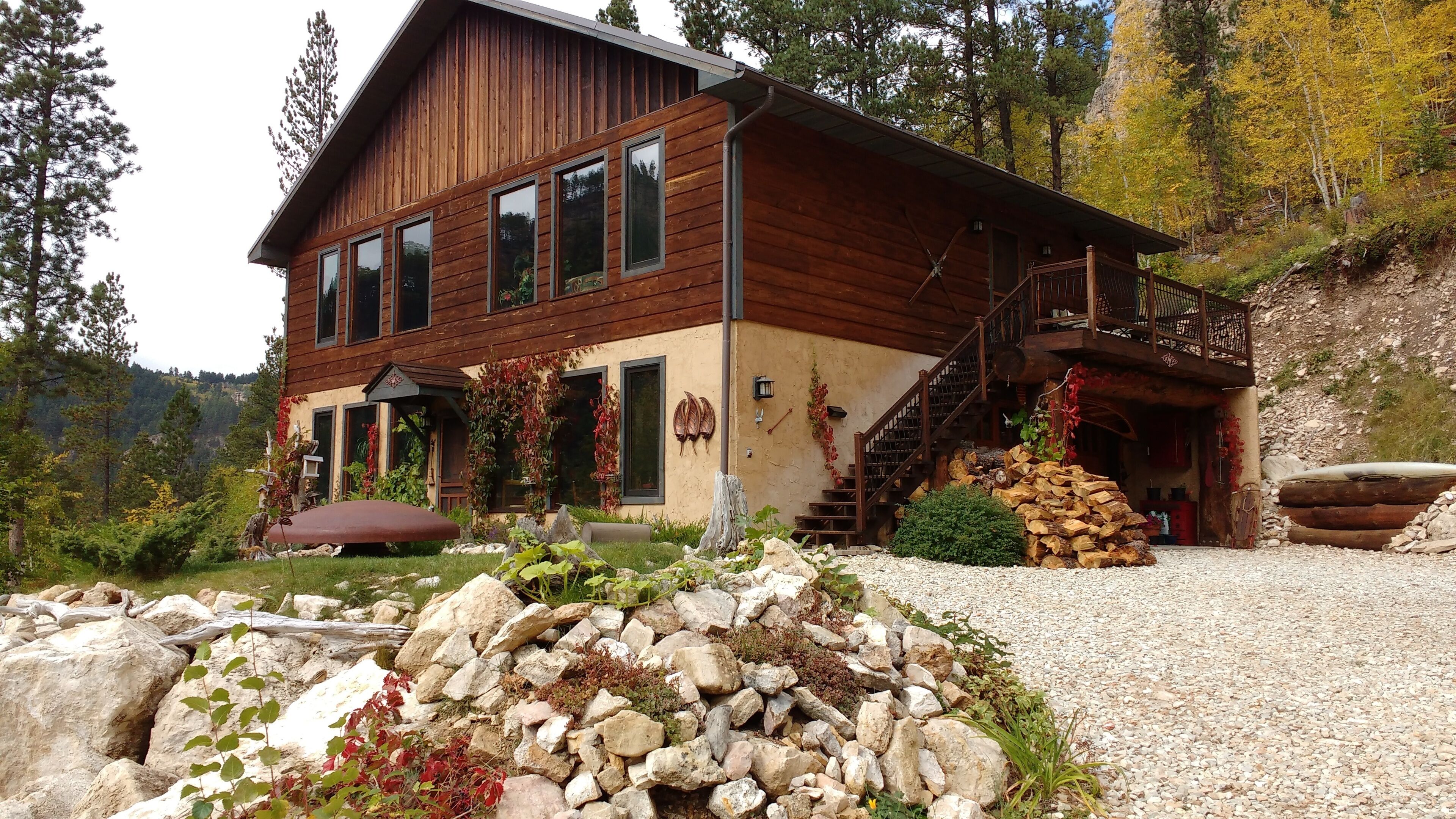 Une cabane en bois dotée d’un balcon, d’un escalier en pierre et d’une pile de bois à l’extérieur.