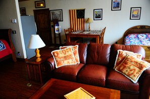 Een gezellige woonkamer met een bruine leren bank, een houten salontafel en een eettafel met stoelen.