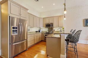 A modern kitchen with stainless steel appliances, a granite countertop, and a bar area with metal chairs.