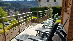 Una terraza de madera con dos sillones de descanso y una mesa, con vistas a una zona residencial con casas y vegetación.
