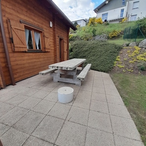 Une cabane en bois avec une table de pique-nique et un banc en pierre.