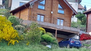 Una casa de madera con garaje cubierto y un coche estacionado en la entrada.