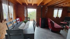 Interior de una cabaña de madera con una mesa de comedor, sillas, un sofá y una chimenea.