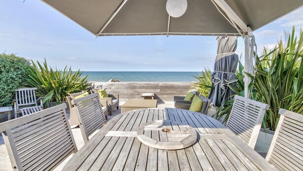 A wooden deck with a round table and chairs, a ceiling fan, and a view of the ocean. - Waterfront house, large terrace and waterfront - Balcony on Arromanches (Asnelles)