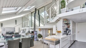 A modern, open-plan living space with a glass dining area, grey furniture, and a kitchen with white cabinetry. - Waterfront house, large terrace and waterfront - Balcony on Arromanches (Asnelles)