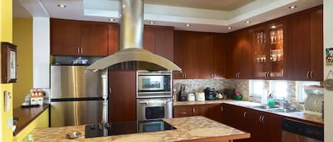 Eine moderne Küche mit Edelstahlgeräten, Holzschränken und einer zentralen Kochinsel mit Barhocker.