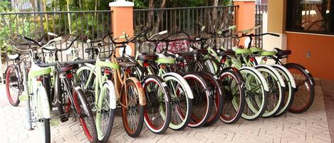 A row of bicycles parked outside a building with a tiled floor and a metal fence.