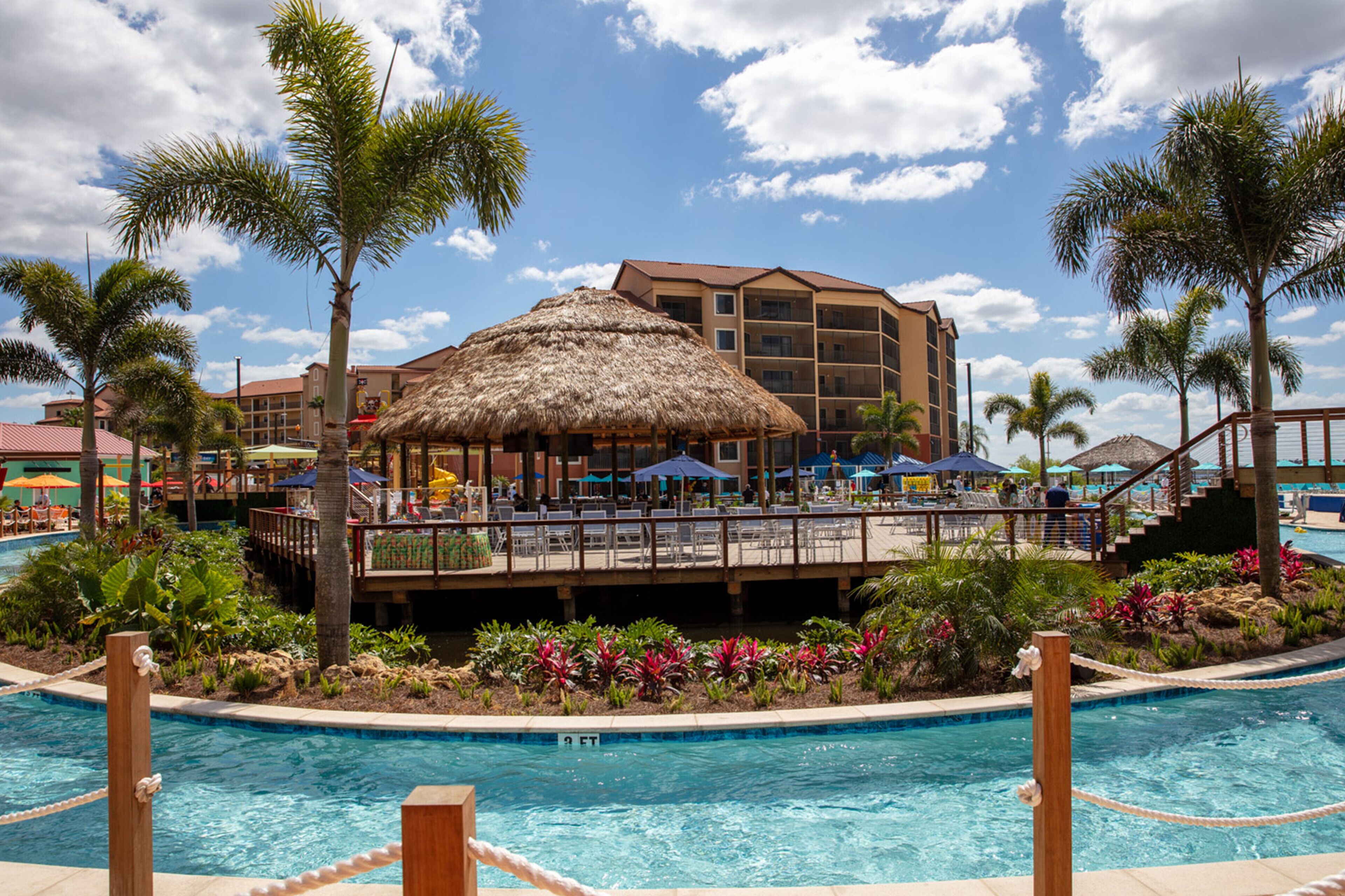 Un hotel con piscina, palmeras y una estructura con techo de paja.