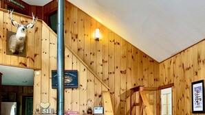 L’intérieur chaleureux d’un chalet avec une cheminée, des murs en bois, un escalier et un ventilateur de plafond.