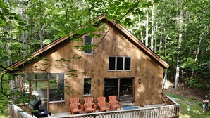 Une cabane en bois dotée d’une terrasse, de grandes fenêtres et de meubles pour s’asseoir à l’extérieur.