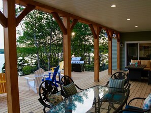 Une terrasse couverte, aménagée avec du mobilier d’extérieur, un barbecue et offrant une vue sur l’eau.