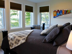 A bedroom with a large bed, a bedside table, a chair, and a window with blinds. - Whitecaps Retreat Beach House (Riverport)