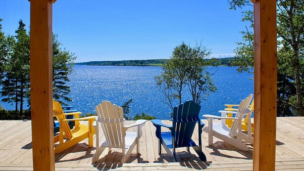 Ett trädäck med Adirondack-stolar som vetter mot en sjö.