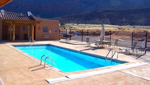 En swimmingpool med udsigt til et bjerglandskab, en overdækket terrasse og et indhegnet udendørs opholdsområde.