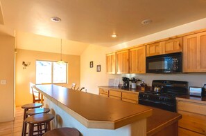 A kitchen with wooden cabinets, a microwave, a stove, and a bar area with stools.