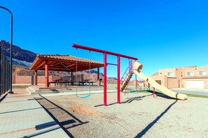 A playground with a slide and swings, a covered seating area, and a mountain backdrop.