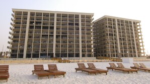 A multi-story hotel with balconies, located on a sandy beach with wooden lounge chairs. - End of Year Special Unit #413 Rates-Beachfront Beautifully Renovated  2/2Sleeps8 (Orange Beach)