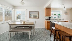 Uma cozinha moderna com área de refeições, destacando uma ilha grande, armários de madeira e uma janela com persianas.