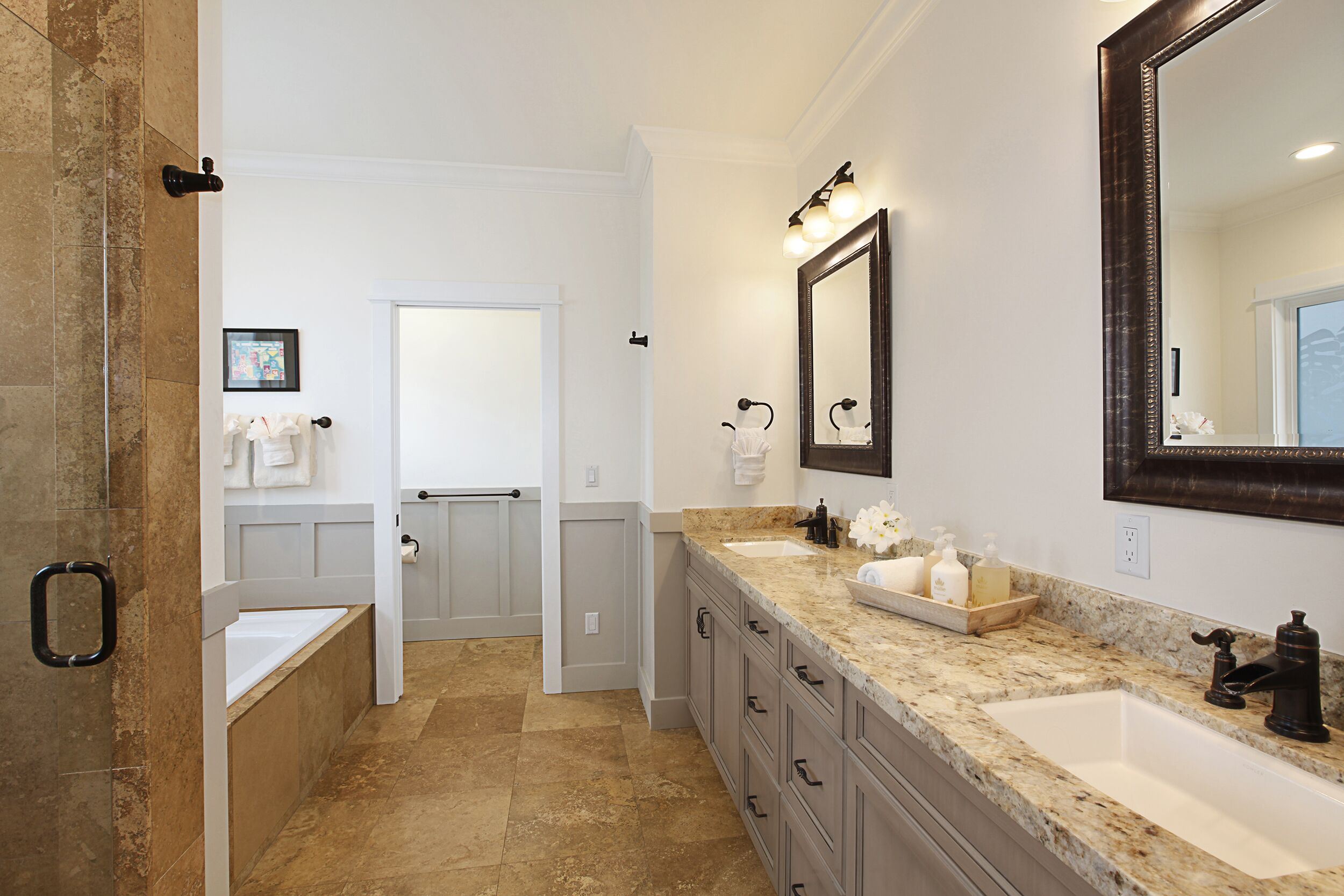 A bathroom with a large mirror, two sinks, a bathtub, and a vanity with drawers.