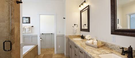 A bathroom with a large mirror, two sinks, a bathtub, and a vanity with drawers.