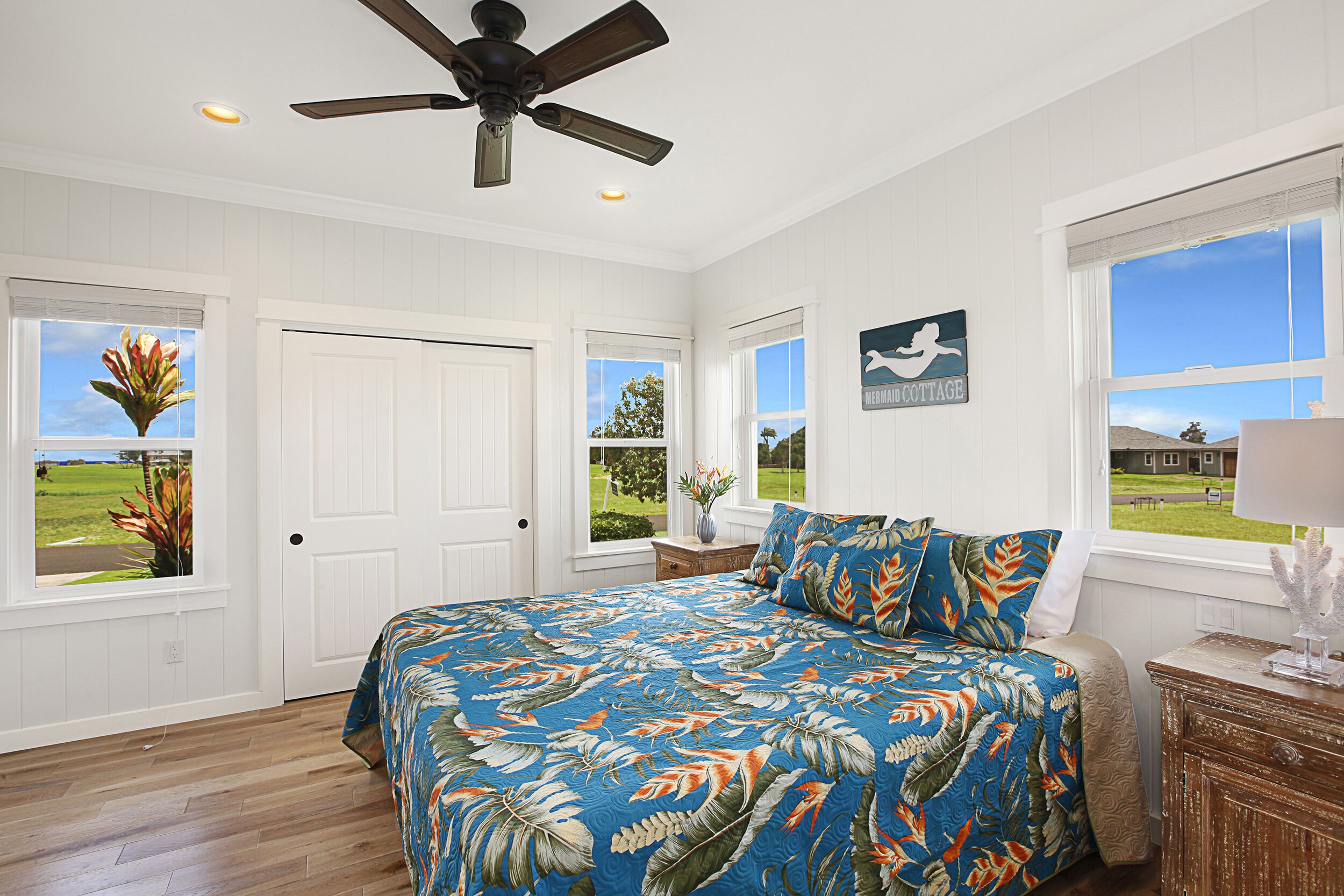 A bedroom with a bed, a ceiling fan, a window with a view, and a door.