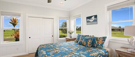 A bedroom with a bed, a ceiling fan, a window with a view, and a door.