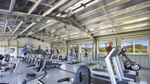 Un gimnasio con diversas máquinas de ejercicio, ventanas amplias y vistas al exterior.