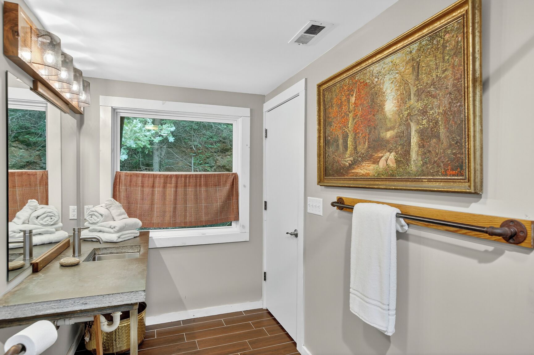 A bathroom with a window, a painting, and a towel rack.