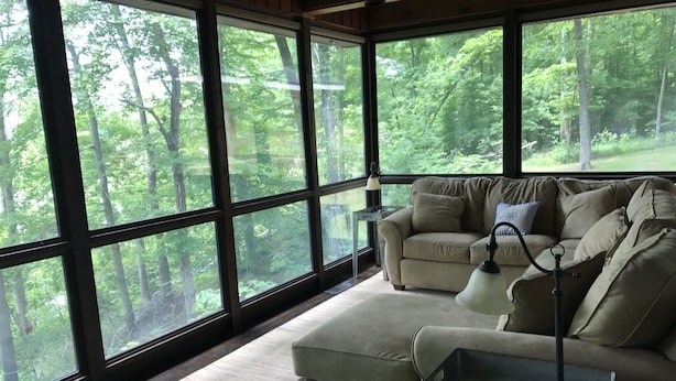 A room with large windows offering a forest view, a beige sofa, a small table, and a lamp. - Year-round 3BR/2BA Lake front - Nolin State Park (1mile) -Mammoth Cave (30min) (Mammoth Cave)