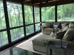 Habitación con amplios ventanales que dan a un bosque, un sofá color beige, una mesita y una lámpara.