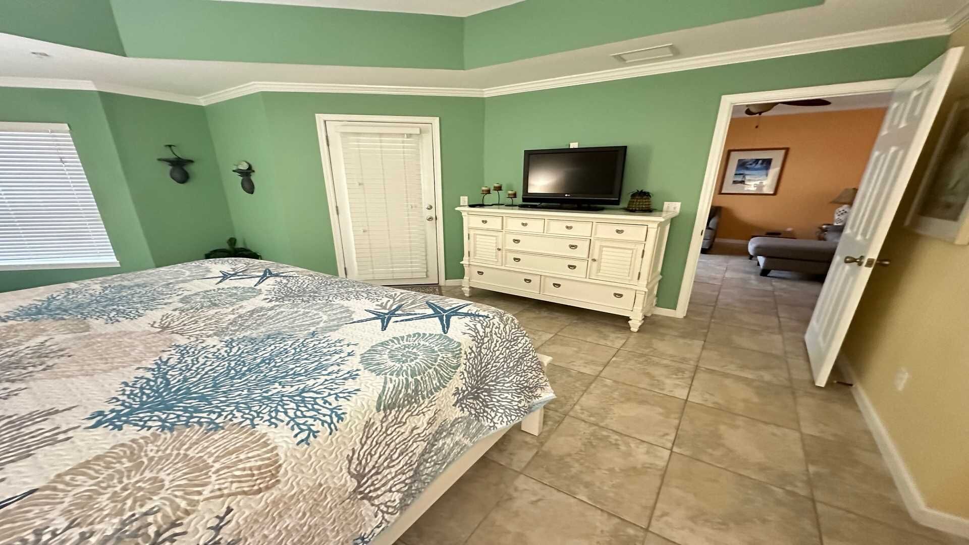 Ein Schlafzimmer mit einem Bett, einem Schminktisch, einem Fernseher und einer Tür zu einem anderen Raum.