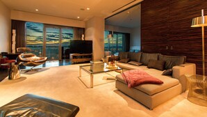 A modern living room with a large flat-screen TV, comfortable seating, and a view of the cityscape through large windows.