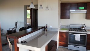A kitchen with a central island, wooden cabinets, a stove, and pendant lighting. - Your Nicaragua Beachfront Hideaway – 2BR at Playa Tesoro (Leon)