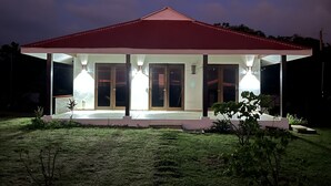 A covered outdoor area with a red roof, glass doors, and illuminated by three lights. - Your Nicaragua Beachfront Hideaway – 2BR at Playa Tesoro (Leon)