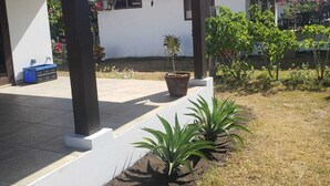A covered outdoor area with a concrete bench, potted plants, and a building with a red roof. - Your Nicaragua Beachfront Hideaway – 2BR at Playa Tesoro (Leon)