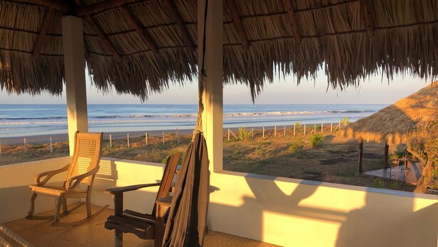 A beachside room with a hammock, two wooden chairs, and a view of the ocean. - Your Nicaragua Beachfront Hideaway – 2BR at Playa Tesoro (Leon)