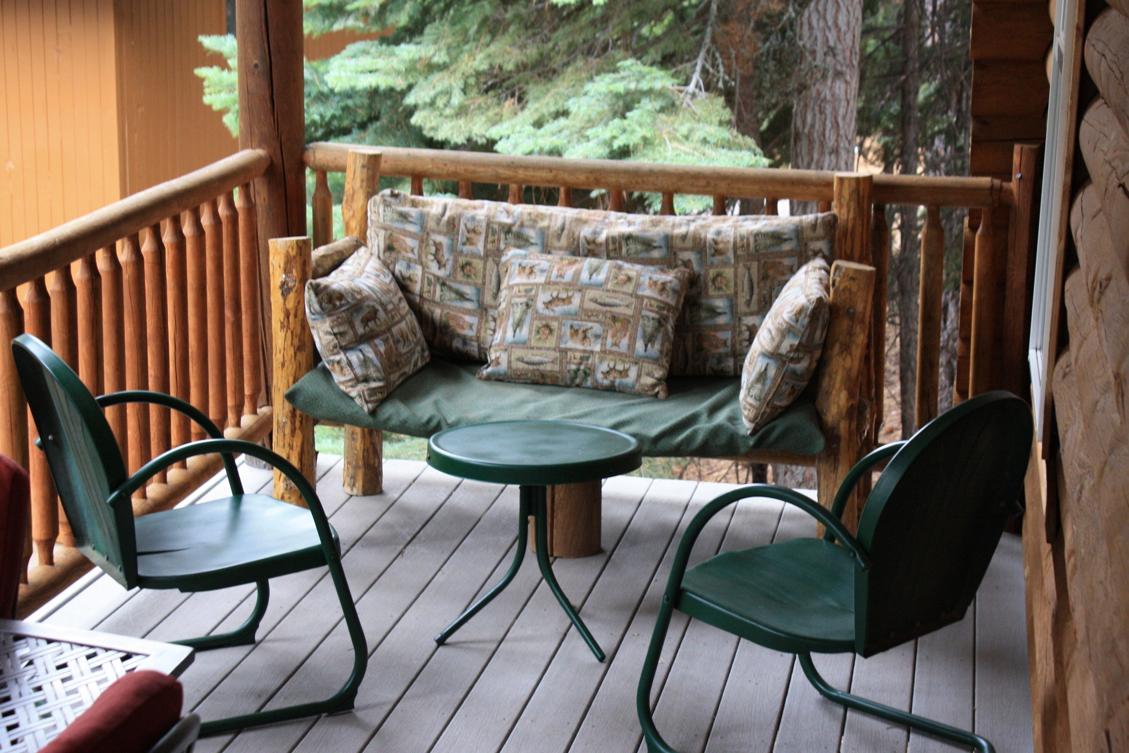 A wooden deck with a green cushioned bench, two green chairs, and a small round table.