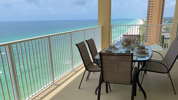 A balcony with a table set for two, overlooking a beach and ocean. - Luxury Ocean Front End Unit. Unobstructed sunset views! Beach service included! (Panama City Beach)