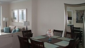 A dining area with a wooden table and chairs, a decorative vase, and a sofa with cushions. - Luxury Ocean Front End Unit. Unobstructed sunset views! Beach service included! (Panama City Beach)