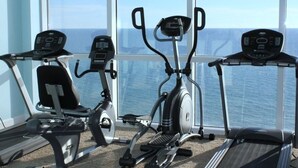 A gym with cardio equipment including an elliptical, a stationary bike, and a treadmill, with a view of the ocean through large windows. - Luxury Ocean Front End Unit. Unobstructed sunset views! Beach service included! (Panama City Beach)