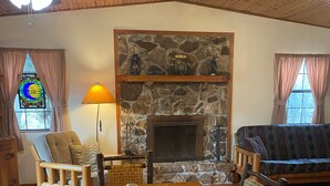 A cozy living room with a stone fireplace, wooden furniture, and a stained glass window. - Beautiful, secluded cabin in the hills of the Ozarks. (birch tree)
