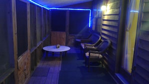 A covered outdoor seating area with a table and chairs, wooden walls, and blue LED lighting. - Beautiful, secluded cabin in the hills of the Ozarks. (birch tree)