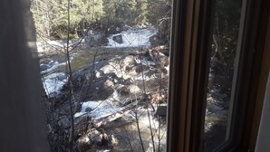 On aperçoit un ruisseau rocheux, des arbres et un plancher en bois à travers une porte vitrée.