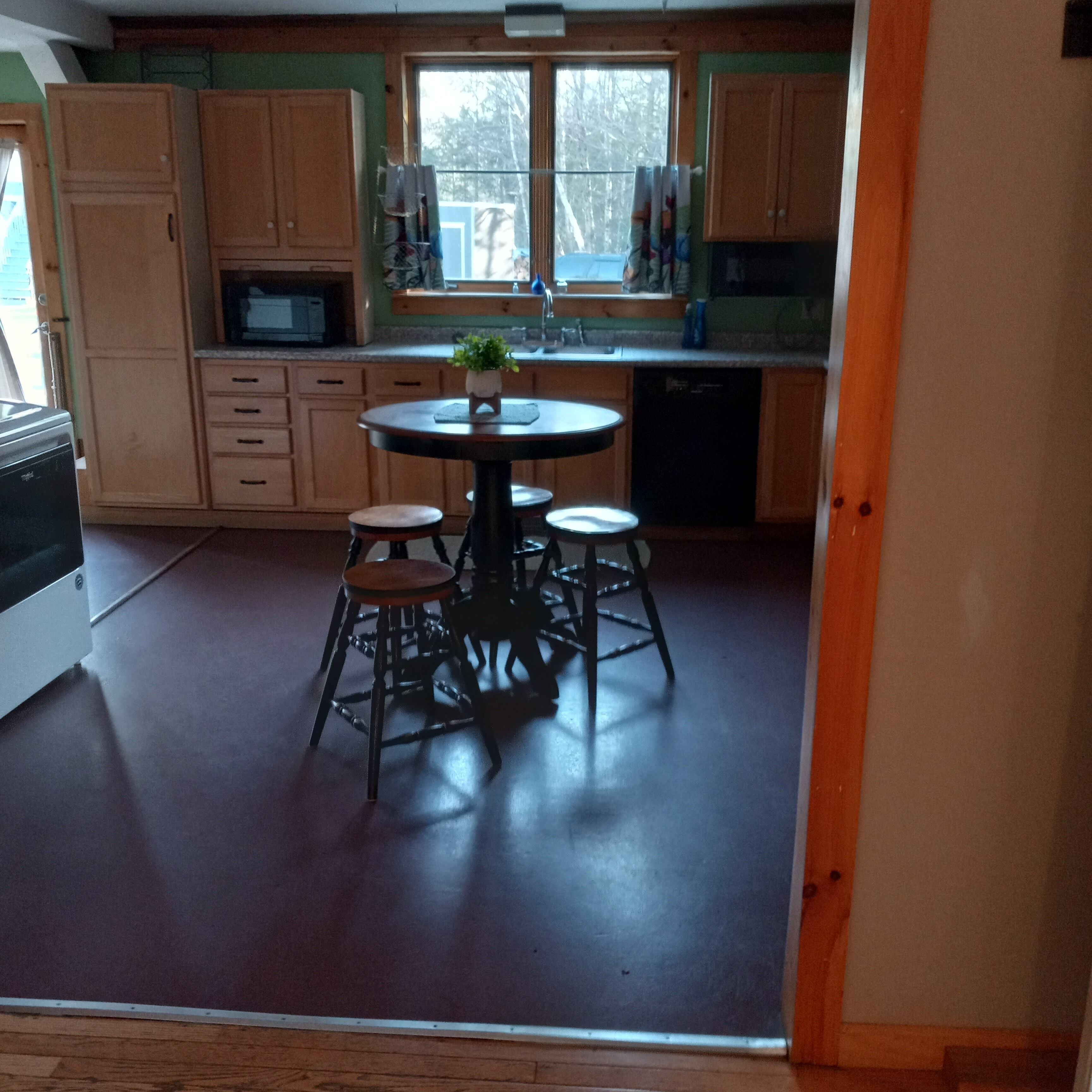 A kitchen with wooden cabinets, a dining table with stools, and a window with curtains.
