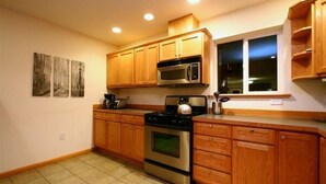 Une cuisine avec des meubles en bois, une cuisinière en acier inoxydable, un four à micro-ondes et une fenêtre avec des stores.